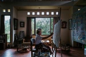 a woman is painting a canvas in a room at Jati Home Stay in Ubud