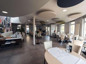 un restaurante con mesas y sillas blancas y ventanas en Aero44 Hotel Charleroi Airport, en Charleroi