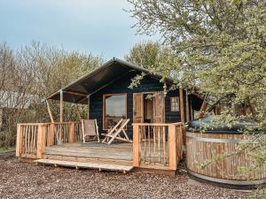 a wooden cabin with a deck and a chair at Smûk Thuskes vlakbij het water in Friesland natuur, ontspanning,houtkachel in Echtenerbrug