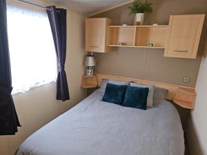 a bedroom with a bed with blue pillows and a window at NEW Orla Caravan in Meliden