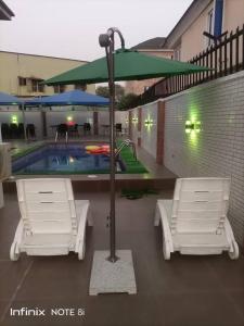 duas cadeiras e um guarda-sol em frente a uma piscina em White Gold Hotel em Ikeja