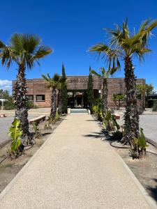 une passerelle avec des palmiers devant un bâtiment dans l'établissement Camping les dunes mobil home 6 personnes, à Torreilles