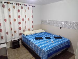 1 dormitorio con cama azul y cortina en POUSADA ALTERNATIVA MANU LAGES Quarto wc comp, en Lages