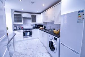 eine Küche mit weißen Schränken, einer Waschmaschine und einem Trockner in der Unterkunft Oxford Street - One Bed Lux in London