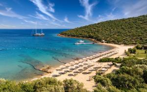 a beach with umbrellas and boats in the water at Kempinski Hotel Barbaros Bay Bodrum in Yaliciftlik