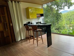 a kitchen with a counter with stools and a large window at Chalé 10 com cozinha próx ao centro in Itatiaia