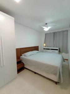 ein weißes Schlafzimmer mit einem Bett und einem Nachttisch in der Unterkunft AP Vista Panorâmica da Praia in Guarapari