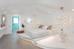 Habitación blanca con cama blanca y lámpara de araña. en Naxos Cave Suites, en Stelida