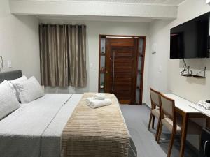 a hotel room with a bed and a desk and a television at Chalé 01 com hidro e cozinha no coração de Penedo in Itatiaia