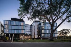 un grand bâtiment en verre avec un arbre devant lui dans l'établissement Element Melbourne Richmond, à Melbourne
