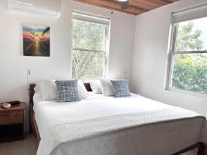 ein Schlafzimmer mit einem Bett mit weißen Laken und zwei Fenstern in der Unterkunft Caribbean Sunrise Cottage in Caye Caulker