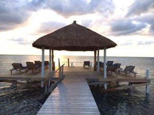 a pier with chairs and a large umbrella on the water at Sea Garden Cottage in Caye Caulker