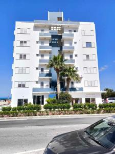 un grand bâtiment blanc avec des palmiers devant lui dans l'établissement 13 Sandy Beach Mackenzie, à Larnaka