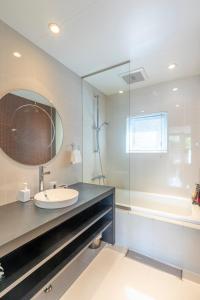ein Badezimmer mit einem Waschbecken, einem Spiegel und einer Badewanne in der Unterkunft Hangetsu Niseko in Niseko