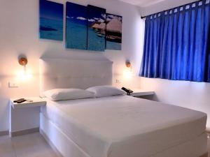 Schlafzimmer mit einem großen weißen Bett und blauen Vorhängen in der Unterkunft Hotel Tropical Inn in Tierra Bomba