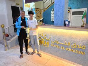 Un uomo in piedi accanto a un ragazzo che tiene un trofeo di hotel khaouni bourdj bou arraredj a Bordj Bou Arreridj