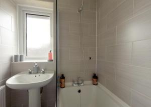 La salle de bains blanche est pourvue d'un lavabo et d'une baignoire. dans l'établissement Voguish 3BR Home in Huyton, à Liverpool