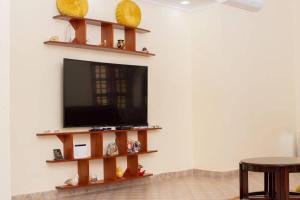 TV de pantalla plana en una pared con estanterías en Hellen's Riverside villas en Moshi