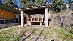 eine Holzbank unter einem Pavillon neben einem Haus in der Unterkunft Ermida Gerês Camping in Ermida