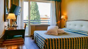 a hotel room with a bed and a desk and a window at Hotel Benaco Garda ***S in Garda