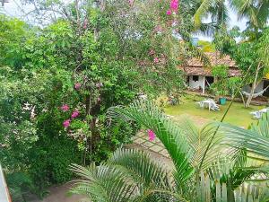 Elle offre une vue sur un jardin avec des fleurs roses et une maison. dans l'établissement Pousada Verdes Mares, à Santa Cruz Cabrália