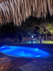 a blue swimming pool at night with a thatched roof at Pousada Velho Bateau in Atins