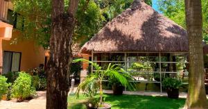 ein Gebäude mit einem Strohdach und Pflanzen auf einem Hof in der Unterkunft Tukan Hotel Playa del Carmen in Playa del Carmen
