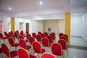 ROSES REGENCY HOTEL AND SUITES في أبوجا: غرفة فارغة مع كراسي حمراء وطاولات وغرفة مع ermetromt