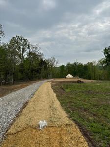 a dirt road with a field and a house in the distance at 10 point landing Mammoth Cave Glamping Sublimity in Horse Cave