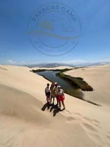 tres personas de pie en la cima de una duna de arena en "Paracas Camp", en Paracas