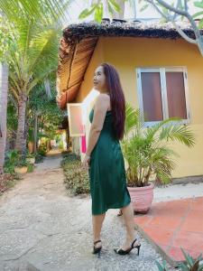 Thuy - Gunter Garden Bungalow في موي ني: امرأة ترتدي ثوب أخضر تقف أمام المنزل