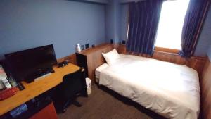 a bedroom with a bed and a desk with a television at Handa Station Hotel in Handa