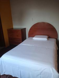 Schlafzimmer mit einem weißen Bett und einem Kopfteil aus Holz in der Unterkunft Cáyamahue Guest House in Pucallpa
