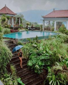 a woman walking down stairs with an umbrella next to a swimming pool at Villa Danu in Kintamani