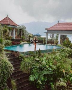 a woman holding an umbrella standing next to a swimming pool at Villa Danu in Kintamani