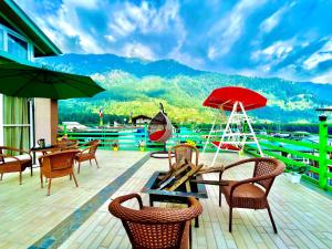 eine Terrasse mit Tischen, Stühlen und einem roten Regenschirm in der Unterkunft Vista Resort, Manali - centrally Heated & Air cooled luxury rooms in Manali