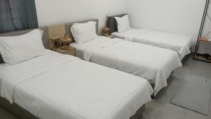 drie bedden in een kamer met witte lakens en kussens bij Three Homestay in Perai