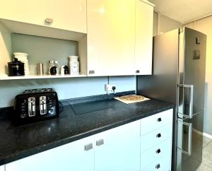 a kitchen with white cabinets and a black counter top at The Standalone - 4 Bedroom Home with Garden by Wild in London