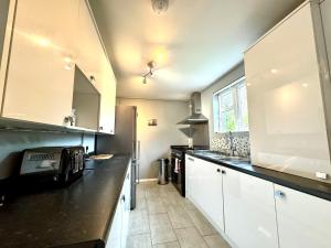 a kitchen with white cabinets and a black counter top at The Standalone - 4 Bedroom Home with Garden by Wild in London