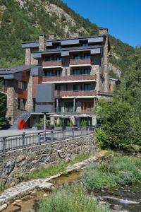 un edificio en una colina con un río delante de él en NH Collection Andorra Palomé, en La Massana