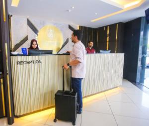 a man standing at a reception counter with a suitcase at Golden Nasmir Hotel Sdn Bhd in Bukit Mertajam