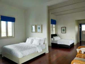 a white bedroom with two beds and two windows at Mahesa 1 in Batu