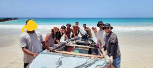 a group of people standing around a boat on the beach at A.M.A Appartament in Calheta Do Maio