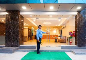 Balwood Suites Near Delhi Airport في نيودلهي: رجل في قبعة التخرج يقف على سجادة خضراء