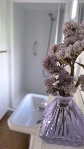 un vaso pieno di fiori viola, seduto accanto a un lavandino. di CasaLola - Corme Porto a La Coruña