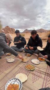 a group of people sitting on the ground eating food at Wadirum sunset camp in Wadi Rum
