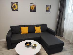 Sofá negro con almohadas amarillas y mesa blanca en Maya's Airport Apartment en Sofía