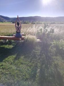 a woman sitting on a bench doing a yoga pose in a field at Gîtes La Musardière in Alba La Romaine