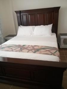 uma cama com uma cabeceira em madeira e lençóis brancos em Rozina Apartments em Nairobi