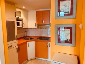 cocina con paredes de color naranja, armarios blancos y fregadero en Apartamentos Rincón del Puerto, en San Vicente de la Barquera